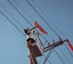 Electrician in a lift repairing overhead power lines on a clear day.