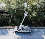 Aerial view of a utility worker on a bucket truck fixing power lines by a road.